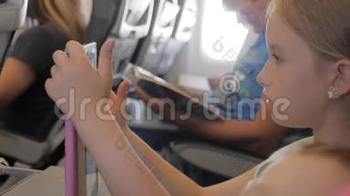 可爱的女孩乘飞机旅行，在飞行中使用数字平板电脑。 与孩子一起<strong>出国</strong>旅行的概念。