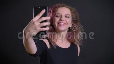 快乐的年轻白种人女孩的肖像，粉红色的头发制作自拍-<strong>照片</strong>使用智能手机在<strong>黑色背景</strong>。