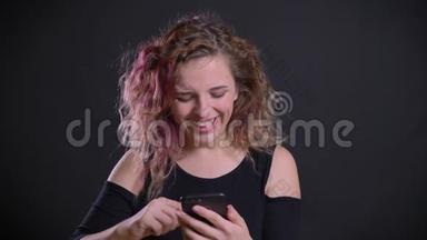 年轻的白种人女孩的肖像，粉红色的头发<strong>看</strong>着她的智能<strong>手机笑</strong>和微<strong>笑</strong>的黑色背景。