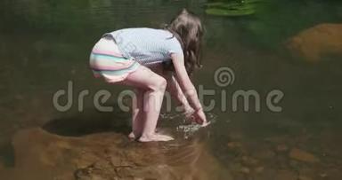 小女孩走上河中的一块岩石，然后弯下腰泼水