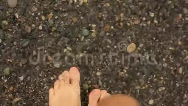 一个人走在鹅卵石滩上，一个人`脚在水里特写。