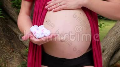 孕妇抱着婴儿袜子，拥抱，拥抱和抚摸怀孕的肚子。 未来的母亲和父母正在等待婴儿。