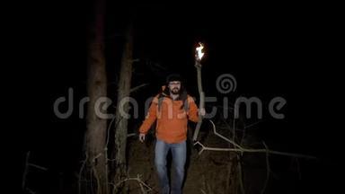 一位游客在树林里迷路了。 一个穿着明亮夹克，手里拿着燃烧的火炬的人在夜晚穿过一个