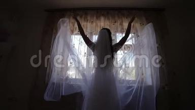 美丽可爱的新娘，穿着婚纱，靠窗<strong>扔下</strong>面纱。婚礼的早晨。漂亮整洁的女人