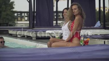 两位穿比基尼的年轻漂亮女士在游泳池附近闲聊，而穿比基尼的男人决定让她们高兴