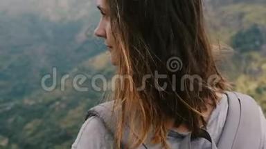 特写镜头在史诗般的山景中，环绕着年轻放松的女人，背包享受着风吹在头发上的风。