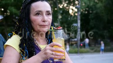 高级奢侈的女人喝着一杯激情水果鸡尾酒，<strong>坐在</strong>公园里的一家街头咖啡馆里，在<strong>树上</strong>。