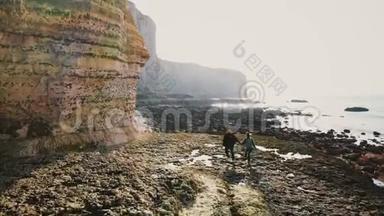 在诺曼底的史诗般的岩石下，一对快乐的游客沿着不可思议的低潮珊瑚和卵石海岸奔跑
