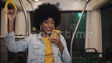 微笑着年轻的非洲裔美国妇女握着扶手，在<strong>公共交通工具</strong>上看智能手机上的视频。 夜晚