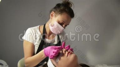 一个非常漂亮的女孩在美容沙龙做一个层压睫毛。 美容师执行手术睫毛