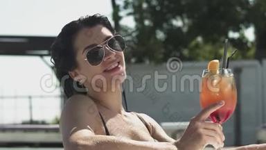 戴太阳镜的漂亮女人在游泳池里摆着鸡尾酒的肖像。 穿<strong>比基尼</strong>的孤独<strong>女士</strong>的休闲。