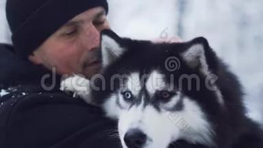 一个穿着冬季外套的男人在户外拥抱和抚摸哈士奇的肖像。带着宠物的家伙。