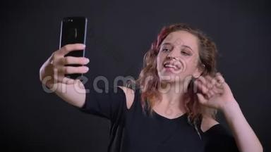 年轻的白种人女孩的肖像，<strong>粉红</strong>色的头发，愉快地在<strong>视频</strong>聊天使用智能手机在黑色背景。
