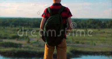 在夕阳下，穿着红色衬衫的孩子背上背着一个背包，在高山上爬到山顶，看着天空中的云彩
