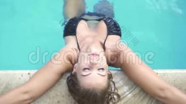 晒黑的女人在避暑胜地的蓝色游泳池里放松。 户外泳池里穿着黑色比基尼的美女