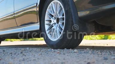 在沥青道路上行驶和滑动的强大汽车车轮的详细视图。 小石头和尘土飞扬
