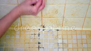 一个女人的手开始清洁一个恶心的淋浴地板，上面覆盖着肥皂渣、霉菌和霉菌