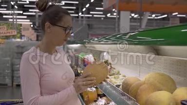 在超市里戴眼镜的年轻孕妇选择新鲜的有机水果。 女人在购物时选择水果。