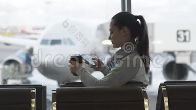美丽的女孩喝外卖咖啡，在机场候机室用电话发信息