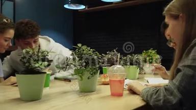 坐在一张有花盆的桌子旁的咖啡馆里，学生们正在看书和聊天。 年轻人的休闲