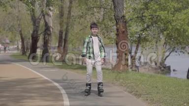 可爱的男孩穿着鲜艳的衣服在河边的公园里滑旱冰。 户外休闲。 一个人玩得开心。 慢慢