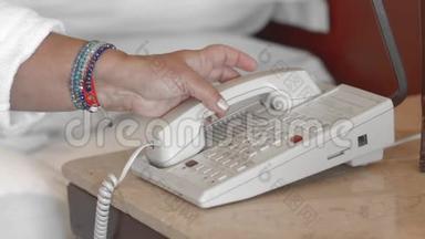 未被认出的穿着白色浴袍的成年高级妇女打电话到酒店房间的接待处，拨电话号码。 慢动作