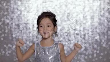 可爱快乐的小女孩穿着<strong>银色</strong>的裙子在<strong>银色</strong>的背景下跳舞。