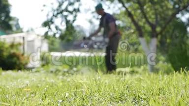在阳光明媚的夏天，用汽油割草机修剪汽车割草机的模糊男工。 在草地上割草
