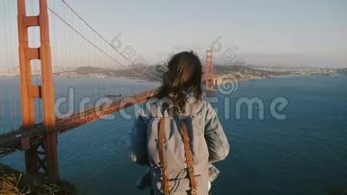 镜头放大年轻幸福的女子背后背包，头发在风中欣赏日落风景在金门大桥。