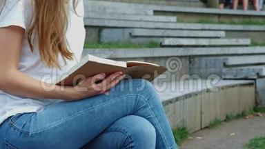 公园里年轻漂亮的女孩正在看书。 一个学生正在学习一本书，<strong>翻页</strong>。 混凝土上的裂缝