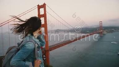 侧观年轻美丽的旅游妇女，背着背包散步，看夕阳的壮丽景色，刮风的金门大桥