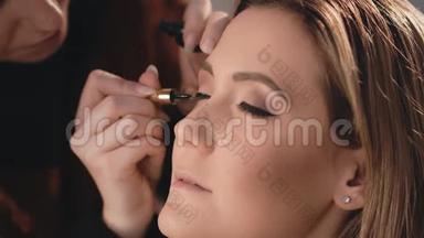 化妆师轻轻地在眼睛的眼皮上放一根黑色的湿眼线，用专业的刷子刷在眼睛的脸上。