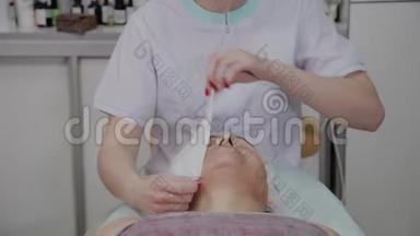 专业美容师从美容办公室的一名老年妇女的脸上<strong>移除</strong>擦拭物。