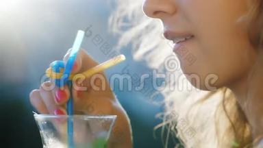 年轻女子在玻璃杯里搅动饮料。 在图片中可以看到阳光照耀的嘴唇和头发。 概念-a