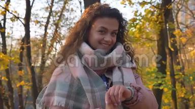 白种人卷发<strong>女人</strong>看着她的<strong>手表</strong>，在秋天公园的背景上转向相机的肖像。
