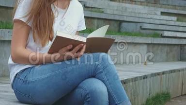 公园里年轻漂亮的女孩正在看书。 一个学生正在学习一本书，<strong>翻页</strong>。 混凝土上的裂缝