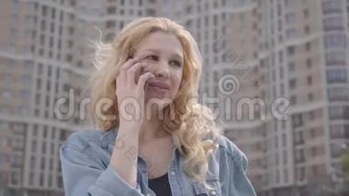 在摩天大楼前用手机说话的漂亮微笑自信的金发女人的特写脸。 城市生活方式