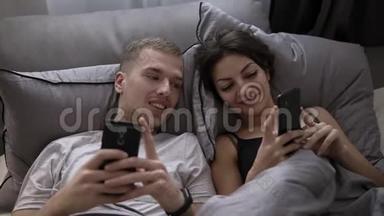 年轻的已<strong>婚</strong>夫妇躺在床上用<strong>手机</strong>互相分享有趣的照片