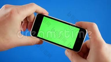 手拿着智能手机玩游戏。 智能手机蓝色背景与绿色屏幕色度。 游戏概念