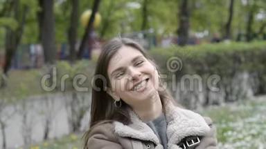 一个非常漂亮的女孩或女人的肖像，她在城市公园里非常情绪化地笑着，看着镜头