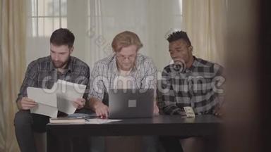 两个高加索人和一个非裔美国人在家休息，坐在笔记本电脑前。 多元文化
