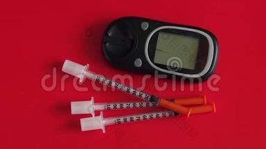 胰岛素注射器和<strong>血糖仪</strong>用于在红色背景下测量<strong>血糖</strong>。