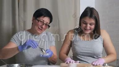 一个怀孕的女孩和她的母亲坐在家里厨房的一张桌子旁，午餐准备饺子和肉末，卷起来