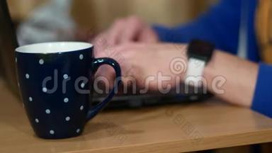 自由职业者正在做笔记本电脑。 在一杯热饮料旁边。 一个人喝茶，脱下智能手表。