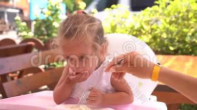 可爱的白人小女孩坐在儿童座椅户外餐厅的桌子上吃意大利面。