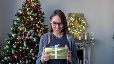 戴眼镜的幸福女人，在装饰好的<strong>家中</strong>，在圣诞树的背景上收到圣诞礼物。 新年快乐