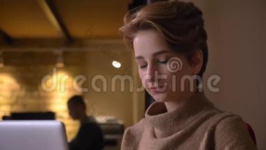 特写照片上忙碌的年轻短发女人，她拿着笔记本电脑，微笑着被办公室里的摄像机分心。