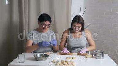 一个怀孕的女孩和她的母亲坐在家里厨房的一张桌子旁，午餐准备饺子和肉末，<strong>卷起</strong>来
