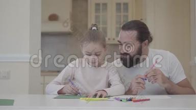 长胡子的男人和小女孩在家里坐在桌子旁用记号笔<strong>画画</strong>。 父亲帮助女儿<strong>画画</strong>，支持