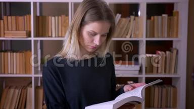 在大学图书馆里，一位年轻有魅力的女学生正在看一本书，看着室内的摄像机